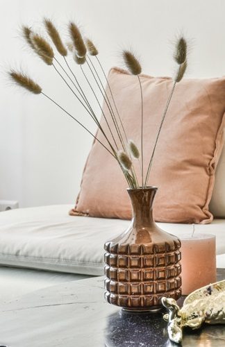 Vase en céramique avec des herbes séchées sur une table près de coussins.