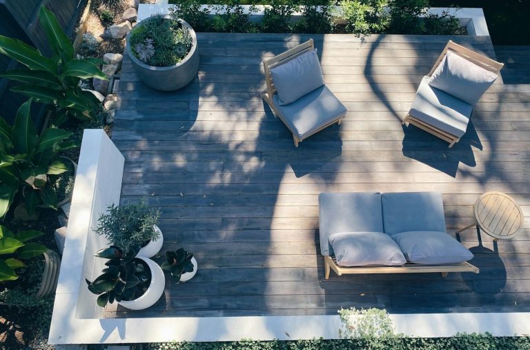 Terrasse en bois avec mobilier relaxant et plantes en pots, éclairée par la lumière du soleil.
