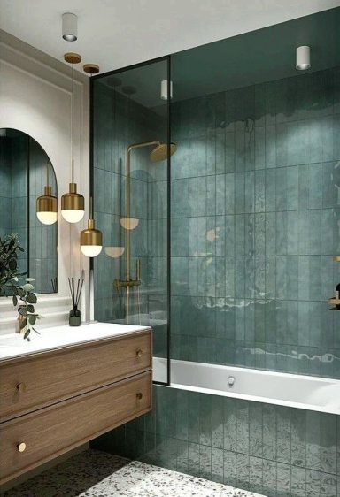 Salle de bain moderne avec carrelage vert, baignoire et éclairage doré.