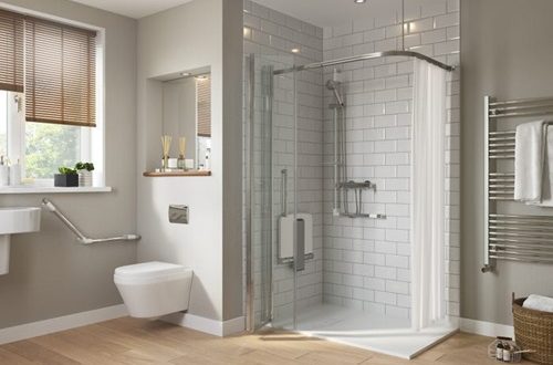 Salle de bain moderne avec douche vitrée, toilettes et accessoires adaptés.
