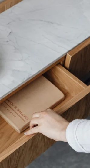 Une main ouvre le tiroir d'un bureau en bois avec un plateau en marbre et un livre à l'intérieur.