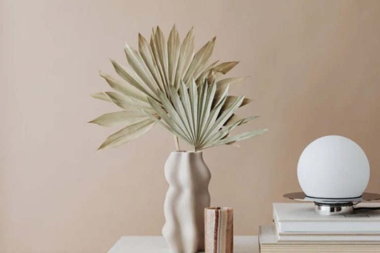 Vase élégant contenant des feuilles de palmier sur une table avec une lampe et des livres.