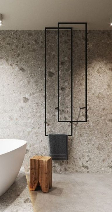 Radiateur design en métal noir sur un mur en pierre, avec une baignoire blanche et un tabouret en bois.