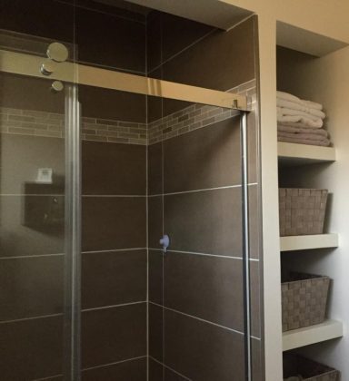 Douche moderne avec paroi en verre et étagères contenant des serviettes et paniers.