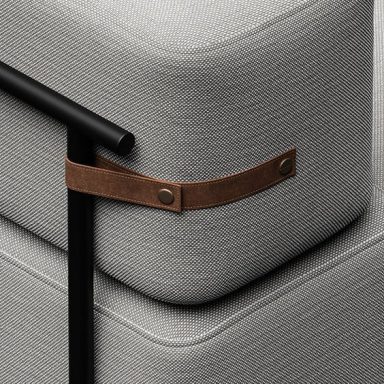 Détail d'un canapé avec un coussin gris et une fixation en cuir brun.