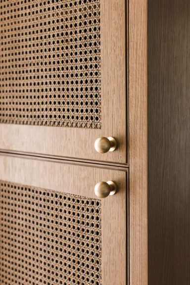 Garde-robe en bois clair avec des poignées rondes et un panneau en cannage.