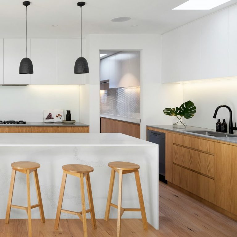 Cuisine moderne avec îlot et chaises en bois, éclairage suspendu et décoration minimaliste.