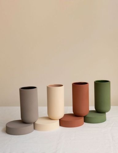 Trois vases de différentes couleurs alignés sur une surface, avec des bases assorties.