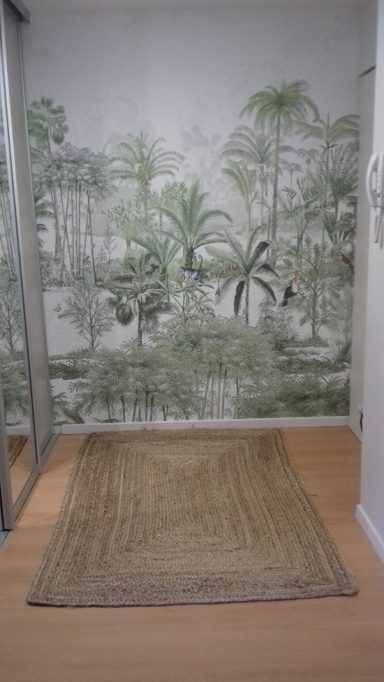 Un couloir avec un tapis, des miroirs et un papier peint de forêt tropicale.