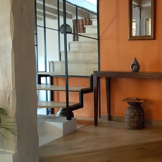 Escalier intérieur avec murs terracotta, table en bois et décoration artistique.