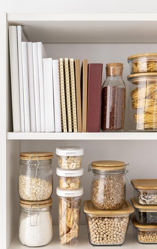 Étagère avec bocaux en verre et livres, contenant des produits alimentaires variés.