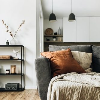 Salon moderne avec un canapé gris, coussins orangés et étagère décorative.