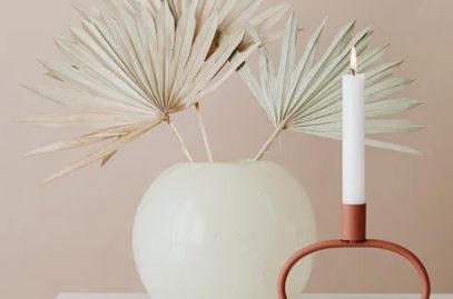 Vase blanc avec des feuilles sèches et une bougie blanche sur un support rouge.