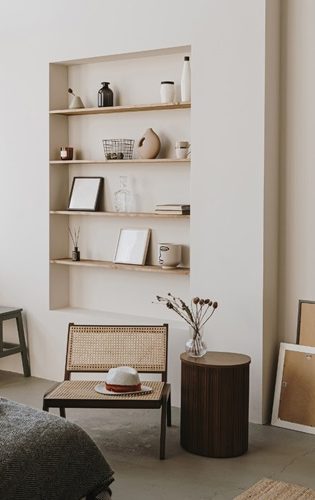 Étagère murale avec objets décoratifs, chaise en rotin et table ronde en bois.
